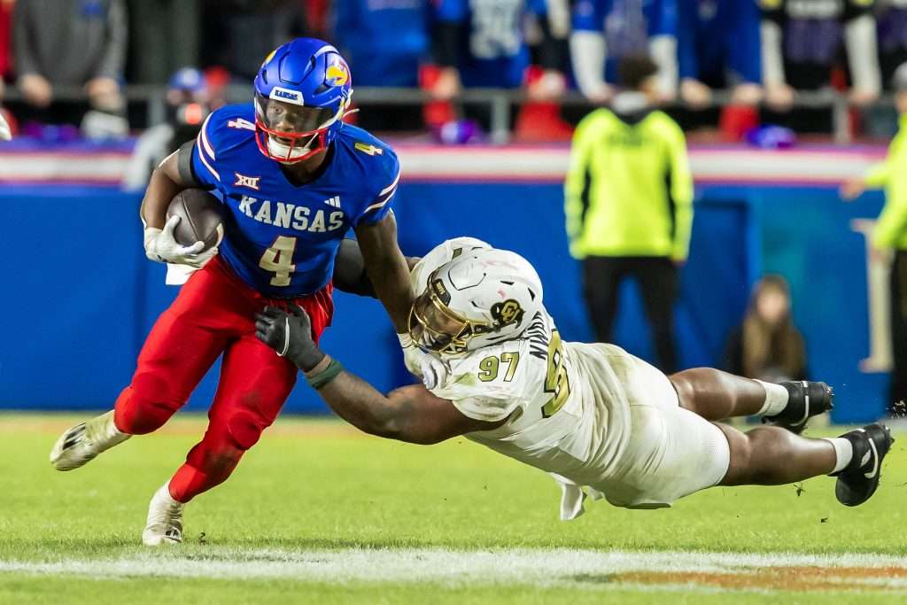 Nov 23, 2024; Kansas City, Missouri, USA; Kansas running back Devin Neal (4) maneuvers past a diving during the Colorado defensive tackle Chidozie Nwankwo (97) in the 4th quarter between the Kansas Jayhawks and the Colorado Buffaloes at GEHA Field at Arrowhead Stadium. Mandatory Credit: Nick Tre. Smith-Imagn Images